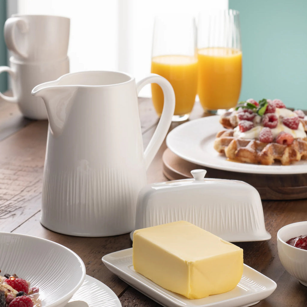 Belleek 9314 Erne Pitcher - Erne pitcher on a wooden table placed beside an Erne butter dish and various pieces of tableware holding sweet treats