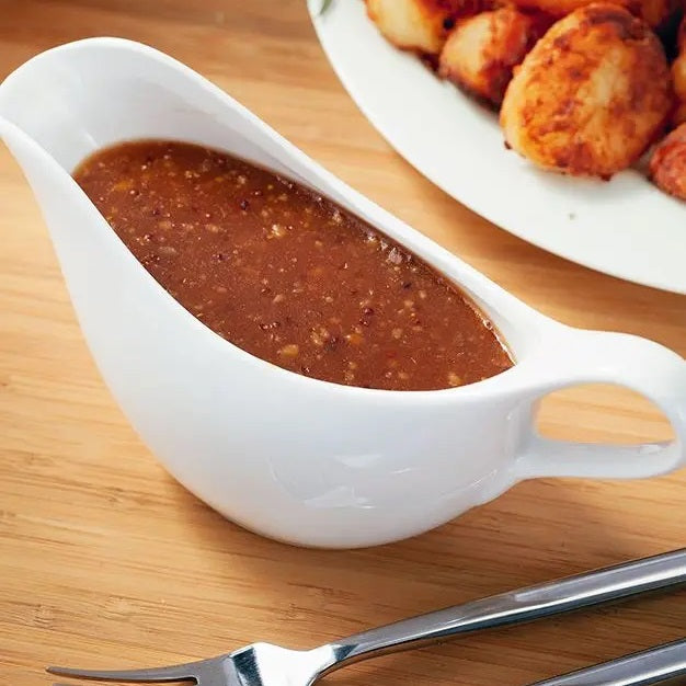 Judge JFY039 500ml Gravy Boat - the gravy boat filled to the brim with gravy pictured on a table with cutlery and roast potatoes