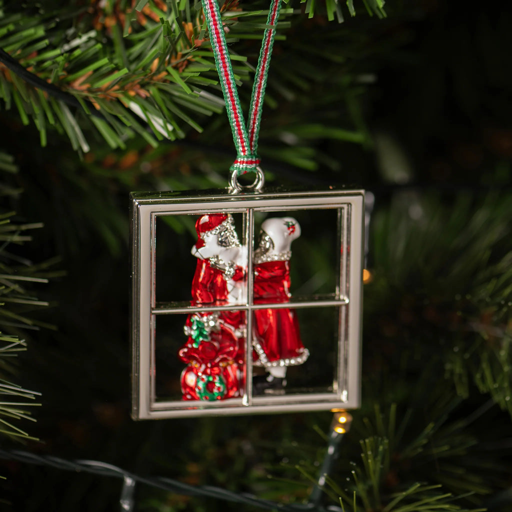 Decorative Christmas ornament with Santa Claus and reindeer in a window frame, hanging on a tree.