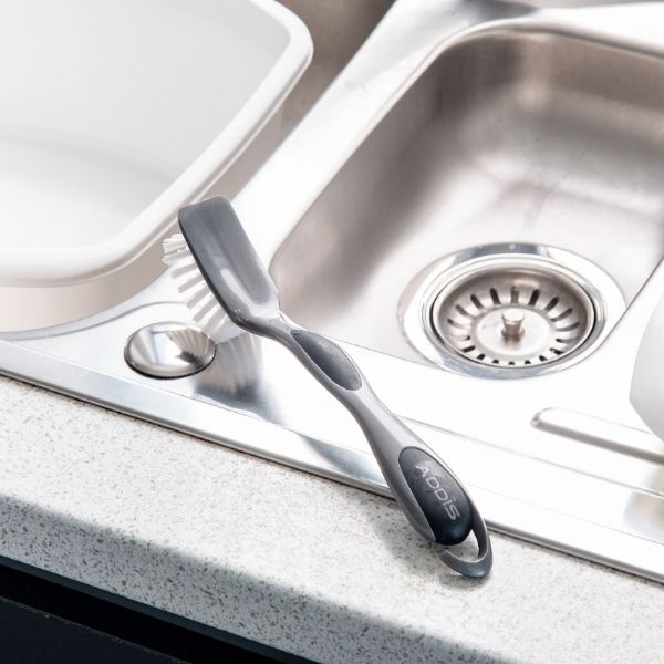 Addis 501131 Dish Brush Bridget Ultra Grip,Metallic sitting on the end of the sink